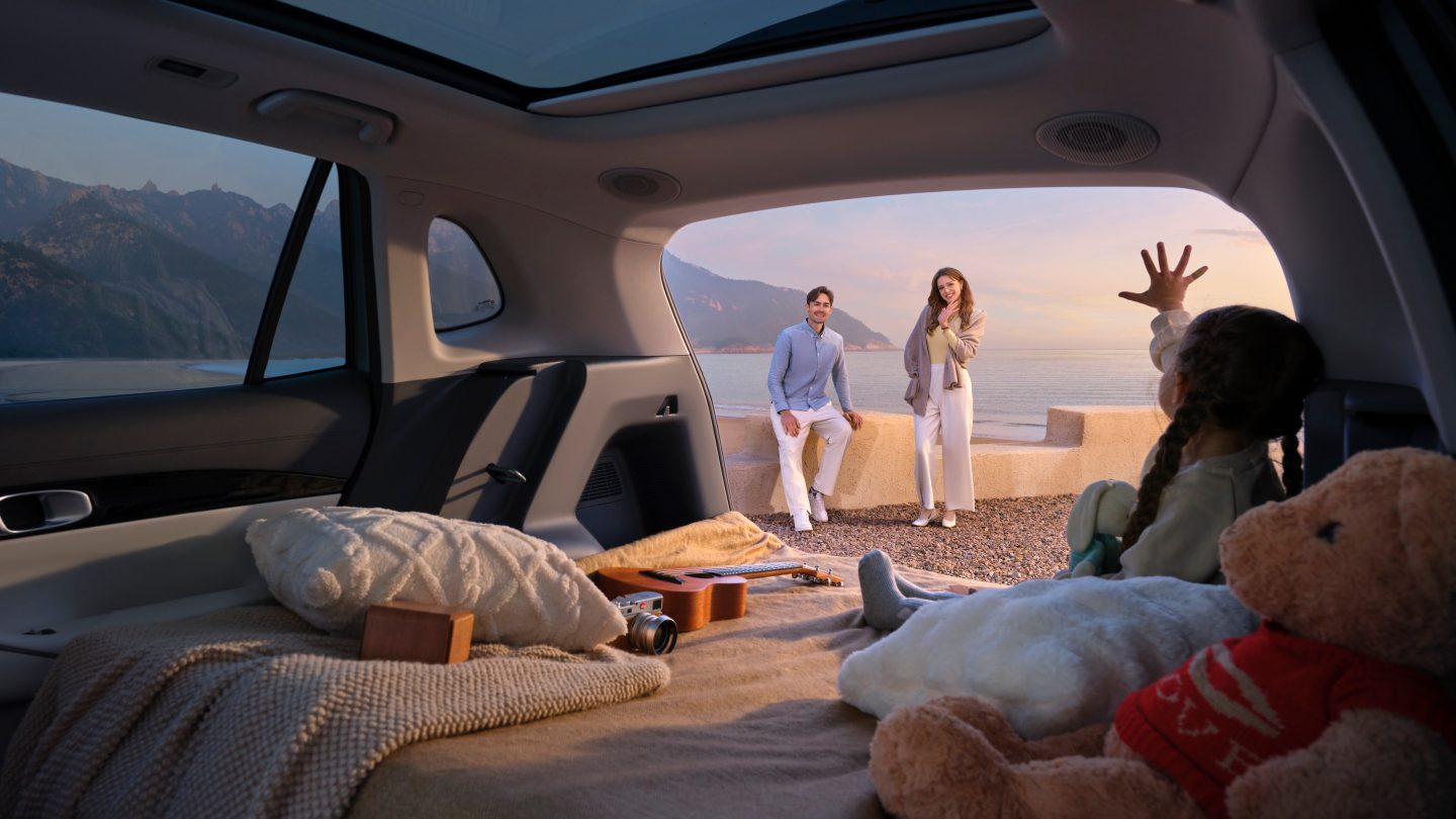 Family relaxing in the open boot of a Geely EX5 by the sea